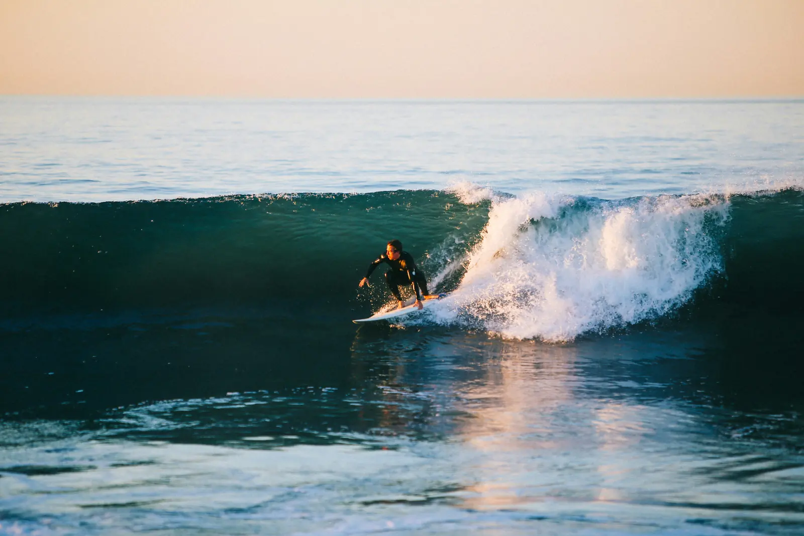 Surfös egy hullám falán naplementében